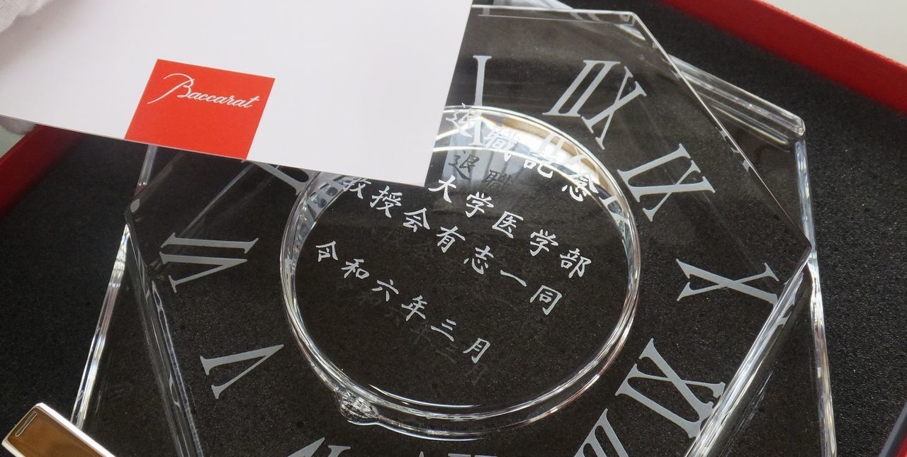 バカラのアビス クロックに、『退職記念 大学医学部 教授会有志一同 令和六年三月』と名入れ彫刻した写真。深海をイメージした重厚なカットが特徴のクリスタル製置時計に、長年の功績を称え、退職を記念するメッセージが丁寧に刻まれています。尊敬する教授の新たな門出を祝福する、記憶に残る特別な贈り物です。