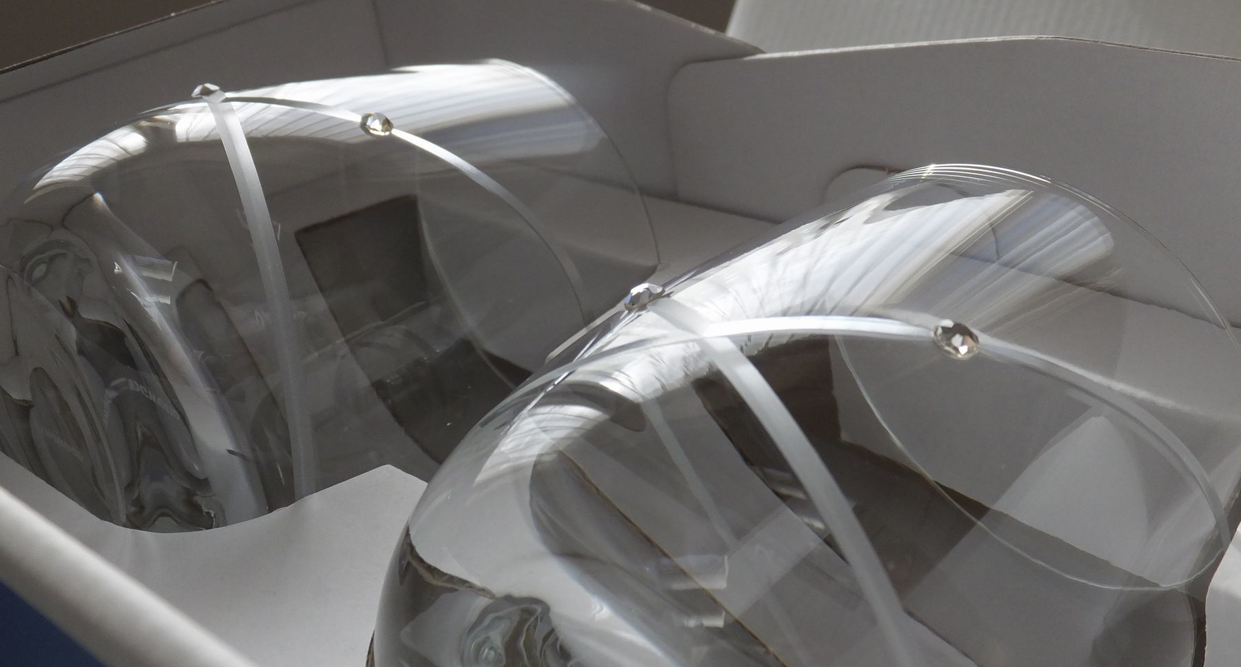 「ウェッジウッド（WEDGWOOD）のクリスタルタンブラー、プロミシス（Promesis） ウィズディスリング リングタンブラーのペアセット（2個）が収められたパッケージ箱の全体写真。箱の表面にはウェッジウッドのロゴと『PROMISES WITH THIS RING』の文字、そして二重のリングカットが施されたグラスのイラストまたは写真が印刷されている。白やクリーム色を基調とした洗練されたデザインの箱が、結婚の誓いと永遠の愛を象徴するギフトの特別感を強調し、完璧な贈答品の状態を伝える情景。