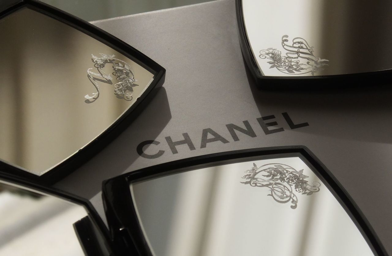バラのデザイン装飾があしらわれたイニシャルが彫刻された3つのシャネルのコンパクトミラー。花びらのように円状に並べられ、エレガントで華やかな特別感を演出したパーソナルギフトのイメージ写真。
