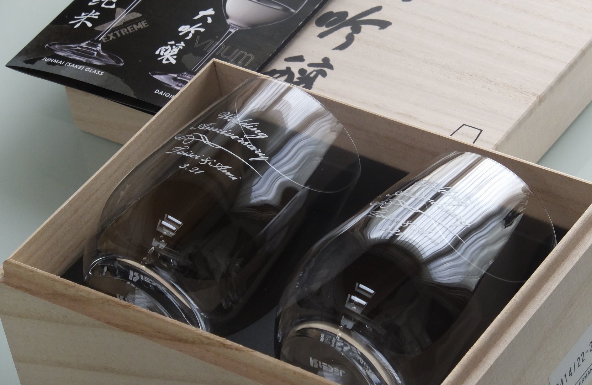 リーデル・オー（RIEDEL O）『大吟醸』グラスの側面に、結婚祝いとして流麗な名入れ彫刻を施した写真。ステム（脚）のないカジュアルで洗練されたタンブラー形状ながら、大吟醸酒の華やかな香りを引き出す卵型クリスタルガラスの側面に、新婚の二人を祝福する文字が精緻に刻まれており、スタイリッシュな暮らしに寄り添う世界に一つだけの特別なウエディングギフトのイメージ。