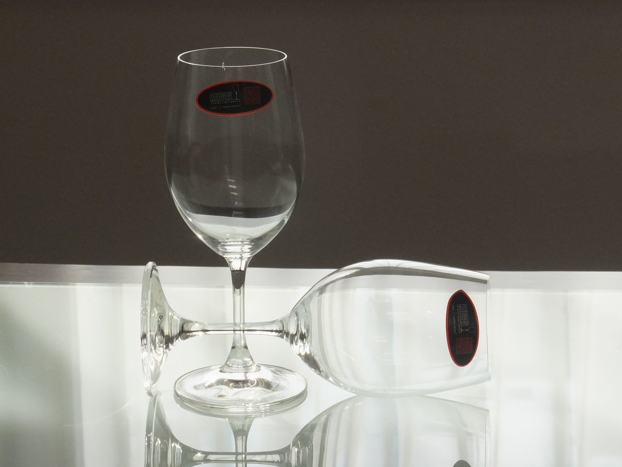 リーデル（RIEDEL）のオーヴァチュア（Overture）シリーズのホワイトワイングラスが、テーブルの上に並べて置かれているペアグラスの写真。機能的で使いやすいデザインが特徴で、すらりとしたボウルと安定感のあるステムが、フレッシュで軽快な白ワインを美しく引き立てている。透明度の高いクリスタリン（またはガラス）が光を柔らかく反射させ、カジュアルながらもエレガントな雰囲気を演出する情景。