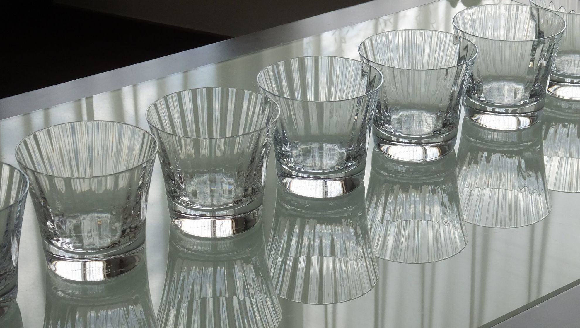 テーブルの上に、バカラ（Baccarat）のミルニュイ タンブラーが7客並べられている写真。千の夜という意味を持つ『ミルニュイ』特有の美しいプリーツ状のカットが光を反射し、多人数でのパーティーや特別な会食を彩る華やかなテーブルセッティングのイメージ。