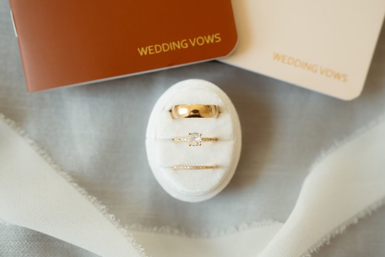 ゴールドの結婚指輪、一粒ダイヤの婚約指輪、ダイヤモンドフルエタニティリング、2枚の結婚の誓いカードが並ぶウェディングフォト