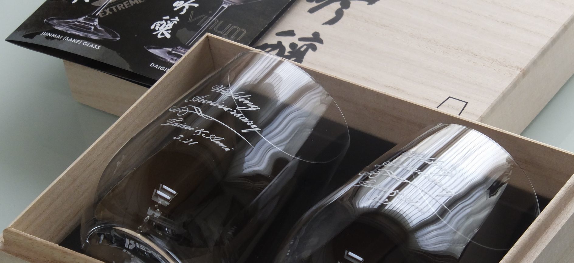 リーデル・オー（RIEDEL O）『大吟醸』グラスの側面に結婚祝いの流麗な名入れ彫刻が施され、格調高い特製木箱に美しく収められた写真。ステム（脚）のない洗練された卵型クリスタルガラスに刻まれた祝福の文字が、木箱の上質な木目と白いインナーサテンに引き立てられて気品高く佇んでいる。特別な日のギフトにふさわしい圧倒的な高級感と、手にした瞬間の贅沢な開封の歓びを伝える世界に一つだけのウエディングギフトのイメージ。