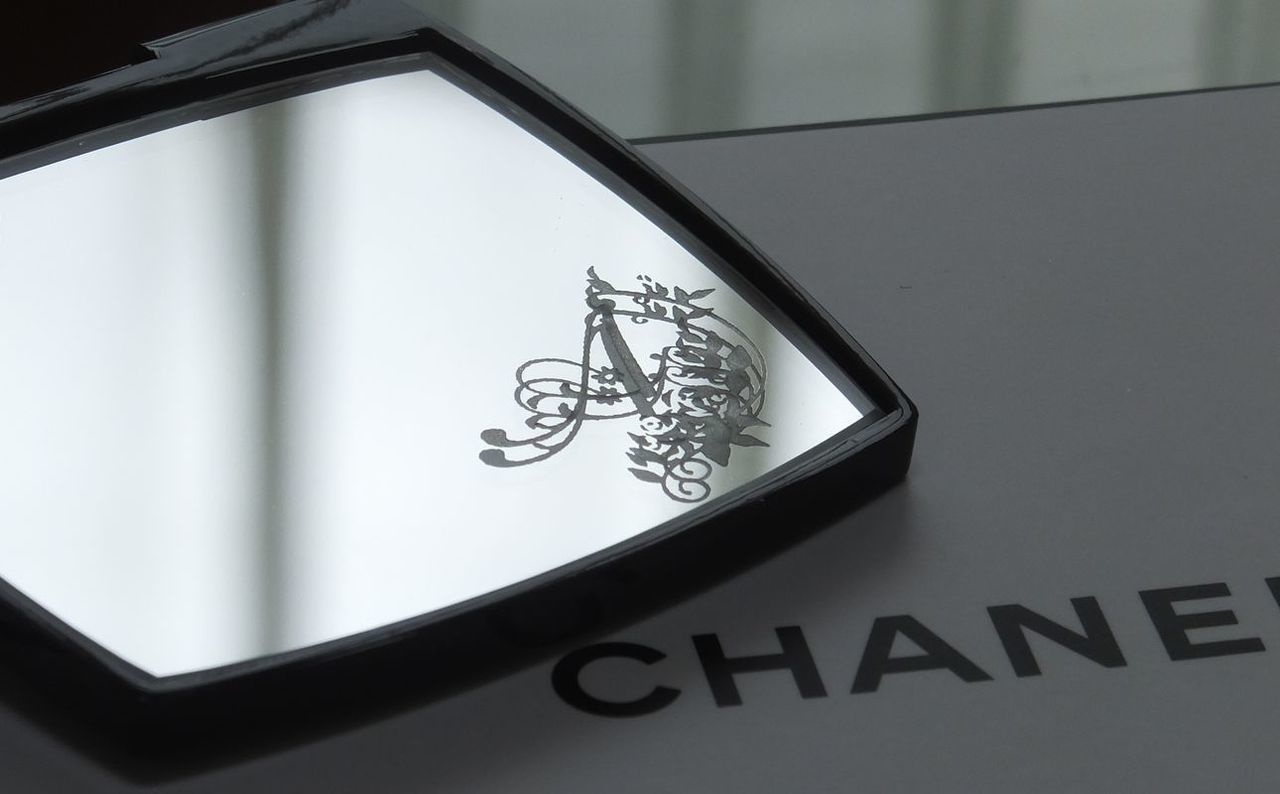 シャネルのコンパクトミラーの下部ミラーに、エレガントなバラの装飾とイニシャル『A』を名入れ彫刻した写真。華やかで繊細なデザインが高級感を醸し出す、特別なギフト仕様のイメージ。