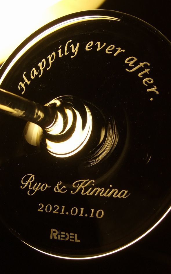 リーデルのグラス底面に施されたオーダーメイドの名入れ彫刻。ご結婚を祝う「Happily ever after」のメッセージと、二人の名前、記念日を刻んだ特別なペアグラス。ご結婚の喜びを美しく演出する最高のギフト
