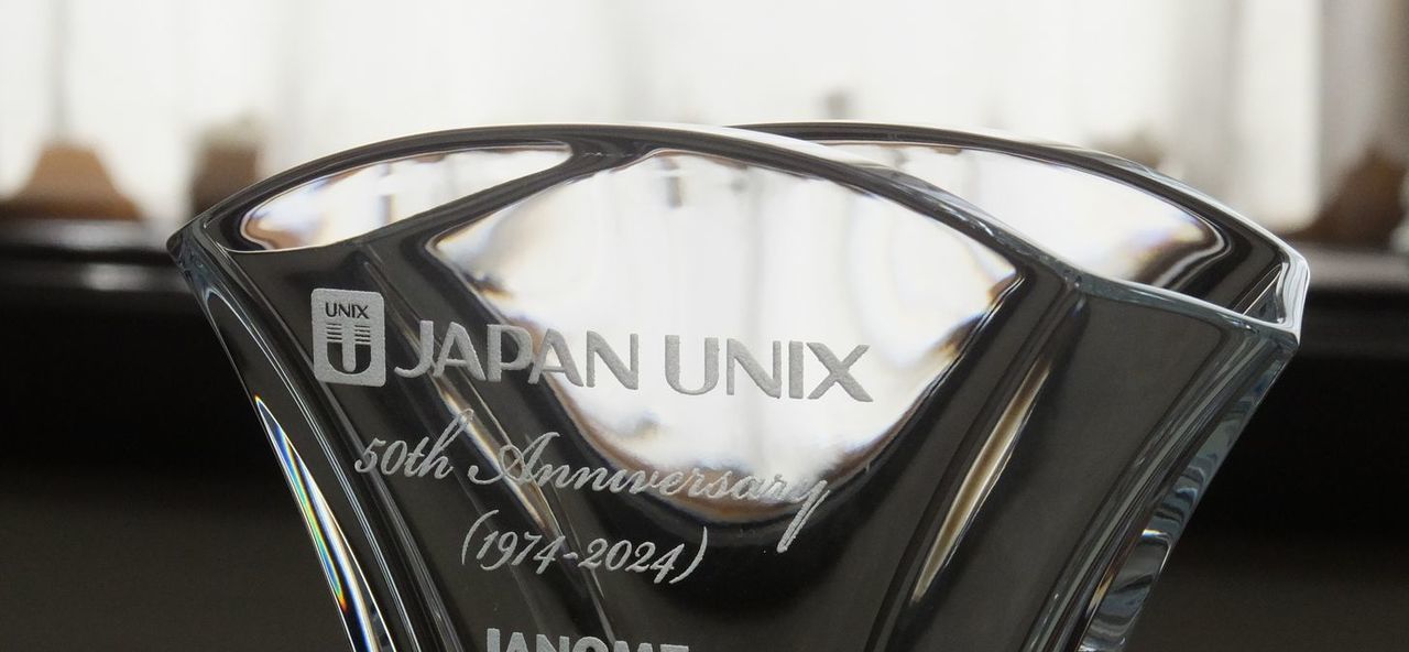 バカラの名入れ花瓶一覧で使用する写真。バカラのギンコベースの側面に、『JAPAN UNIXのロゴデザインと50th Anniversary』を名入れ彫刻した写真。イチョウの葉をモチーフにした優美なデザインのベースに、企業のロゴと50周年を祝うメッセージが格調高く刻まれ、企業の歴史と未来を象徴する特別な記念品です。
