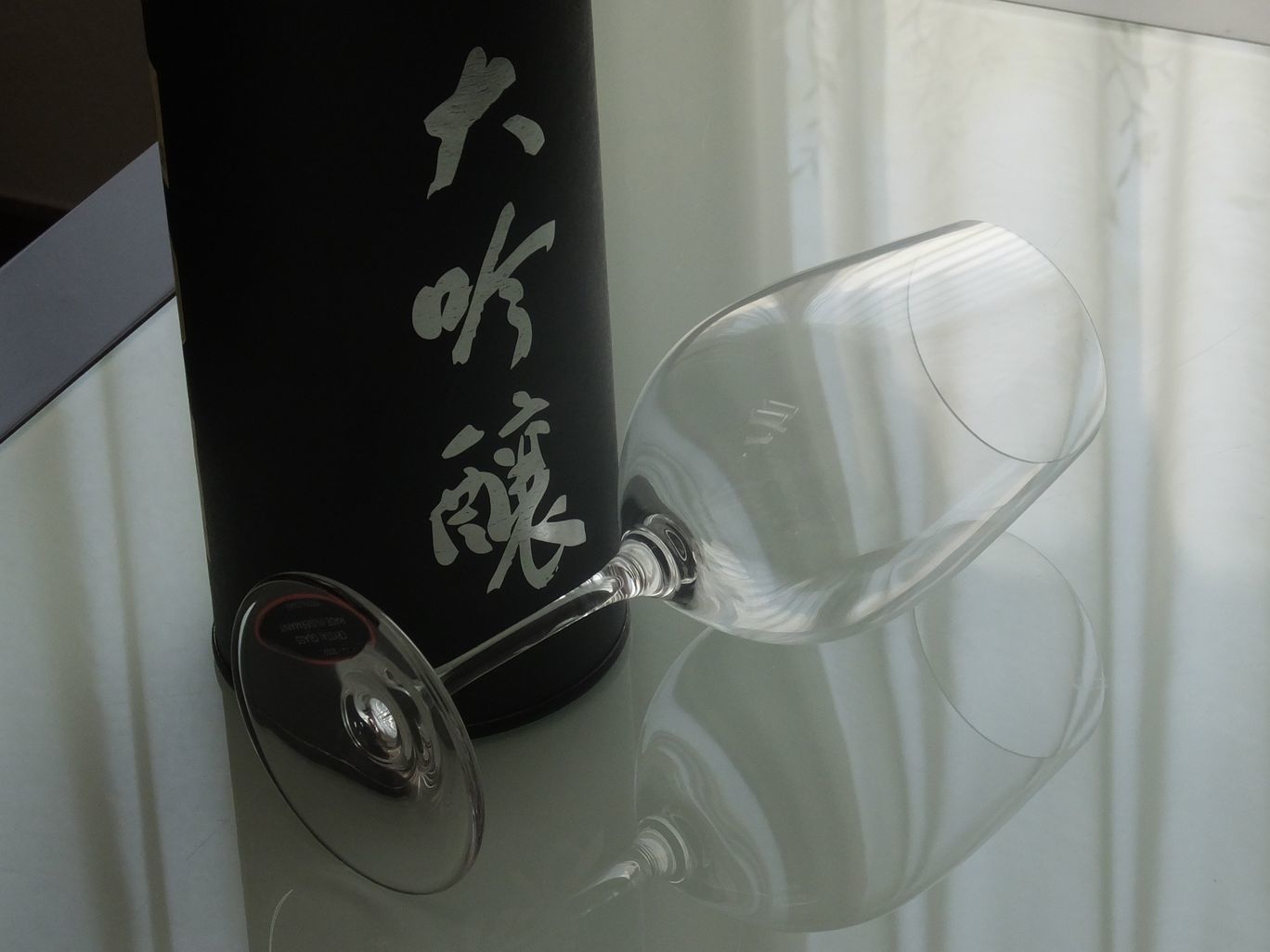 テーブルの上に置かれたリーデル（RIEDEL）『ヴィノム・シリーズ』の大吟醸グラスの写真。大吟醸酒のフルーティーな香りを引き出すために計算された縦長の卵型フォルムが、クリスタルガラスの清澄な輝きとともに美しく際立つ。日本酒の繊細な個性を最大限に楽しむためにデザインされた、機能美あふれる最高級酒器のイメージ。