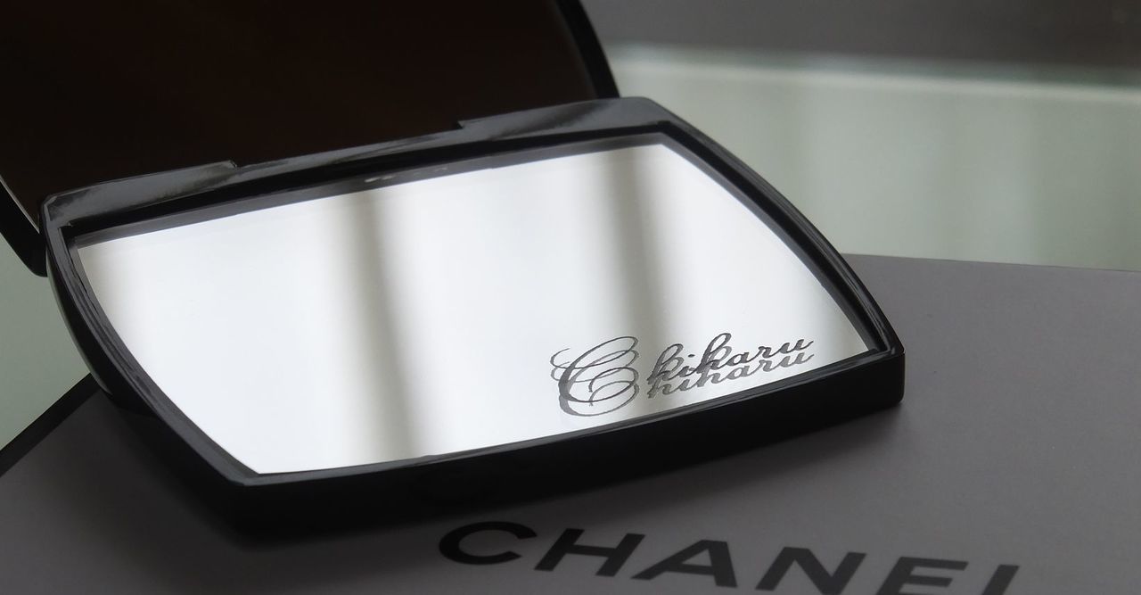 シャネルのコンパクトミラーの下部ミラーに『Chiharu』と名入れ彫刻が施された写真。ギフトでのオーダーをイメージさせる、洗練されたパーソナライズアイテムの紹介。