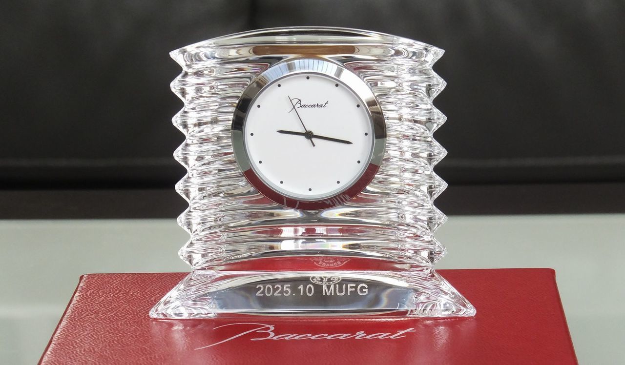 バカラの置き時計、ラランドクロック（Lalande Clock）のクリスタル製クロックのクローズアップ写真。アール・デコ調の優美なフォルムを持つ時計の下部に、『2025.10 MUFG』という企業名と記念日が名入れ彫刻されているのが鮮明に確認できる。繊細なダイヤモンドカットが施されたラランドクロックが、企業の特別な記念や永年勤続表彰などにふさわしい格調高い輝きを放つ法人向け記念品