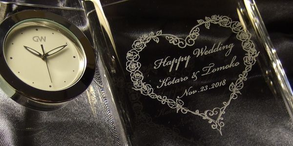 グラスワークスナルミのディクショナリークロックに、バラの花でかたどったハートの中に『Happy Wedding』とお二人の名前、記念日を名入れ彫刻。結婚の思い出を美しく刻む、上質で華やかなメモリアルギフト