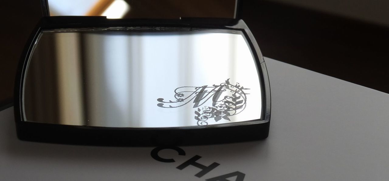 シャネルのコンパクトミラーの下部ミラーに、エレガントなバラの装飾とイニシャル『M』を名入れ彫刻した写真。華やかで繊細なデザインが高級感を醸し出す、特別なギフト仕様のイメージ。