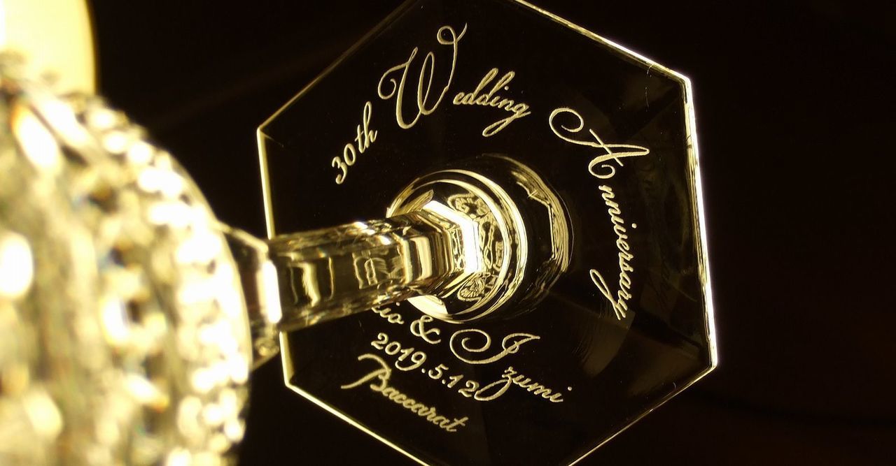 バカラのシャンパングラス、アルクール イブ シャンパングラスの底面に、『30th Wedding Anniversary 二人の名前 2019.5.12』などを名入れ彫刻したアップ写真。象徴的なアルクールデザインのグラスの底に、結婚30周年を祝う特別なメッセージと記念日が繊細に刻まれ、特別な贈り物としての価値と、永続的な愛を象徴する美しさを際立たせています。