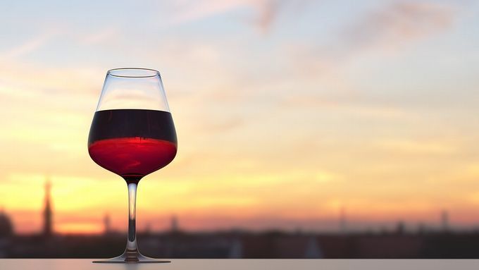 夕暮れの街並みを一望できる場所に置かれたワイングラス。赤ワインの深い色と景色が溶け合い、優雅で穏やかな時間が流れるような一枚