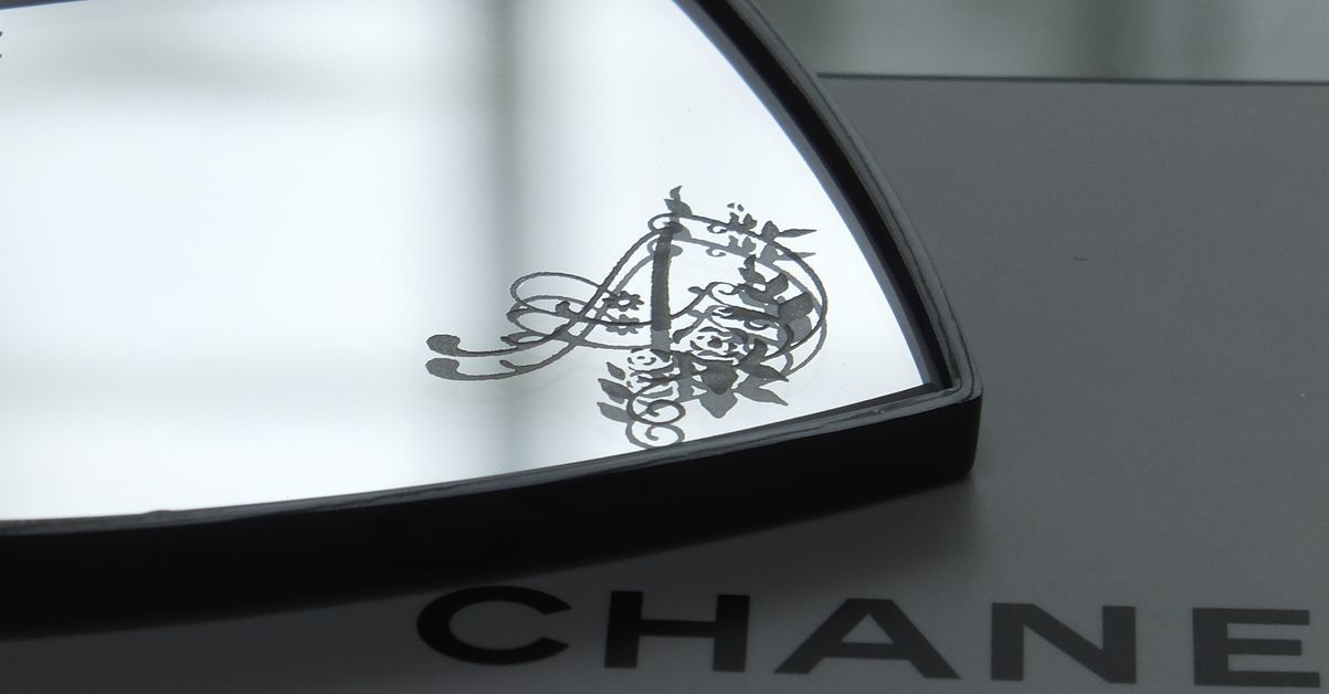 シャネルのコンパクトミラーの下部ミラーに、エレガントなバラの装飾とイニシャル『A』を名入れ彫刻した写真。華やかで繊細なデザインが高級感を醸し出す、特別なギフト仕様のイメージ。