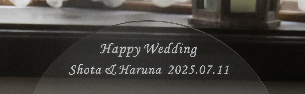 グラスワークスナルミのクリスタル製のドームフォトフレーム（写真立て）のクローズアップ写真。緩やかなアーチを描くクリスタルの正面または下部に、結婚祝いのメッセージとして**『Happy Wedding Shota & Haruna 2025.07.11』という新郎新婦の名前と記念日が名入れ彫刻されているのが鮮明に確認できる。透明度の高いクリスタルが光を反射し、幸せな瞬間を収めた写真とともに、永遠の愛の誓いを象徴するエレガントな記念品。