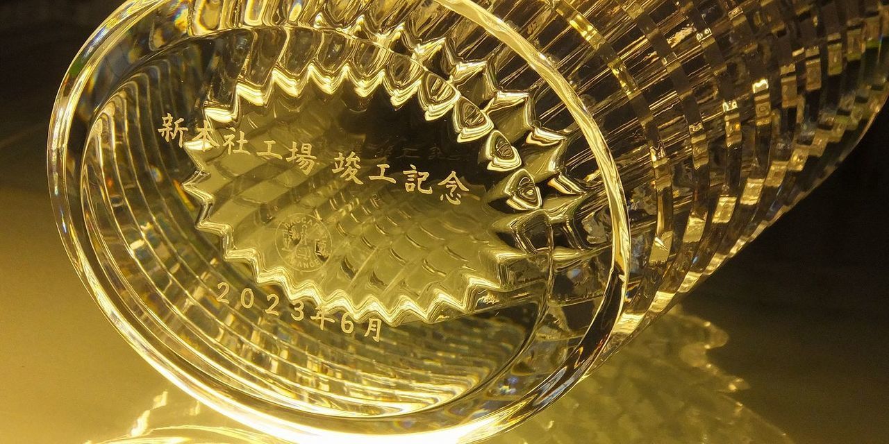 バカラの名入れ花瓶一覧で使用する写真。バカラのアイベースMサイズの底面に、『新本社工場 竣工記念 2023年6月』と名入れ彫刻した写真。光の反射が美しいアイベースの底に、新たな歴史を刻む企業の記念メッセージが繊細に刻まれています。竣工記念品としての高級感と、未来への希望を象徴する、洗練された逸品です。