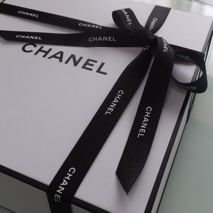 シャネルのギフトボックスに、ブランドを象徴する黒いシャネルのリボンが美しく結ばれているアップの写真。細部までこだわり抜かれたパッケージが、贈り物としての高級感と特別感を際立たせています。