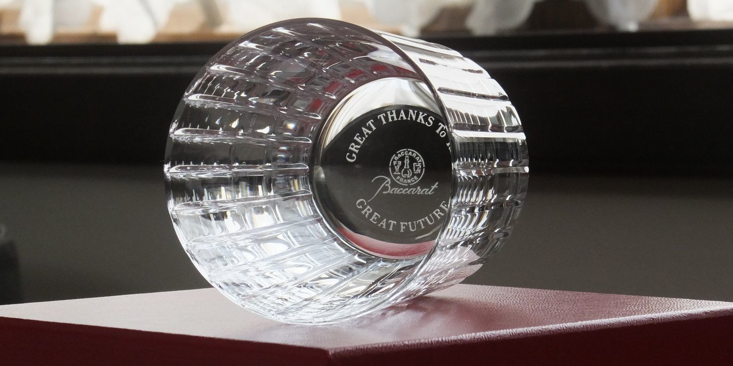 バカラの『ハーモニー』タンブラーの底面に、『GREAT THANKS to TAKE GREAT FUTURE』というメッセージを精緻に名入れ彫刻した写真。垂直のカッティングが特徴的なグラスの底に、感謝と未来への願いを込めた文字がクリスタルの透明感の中で美しく浮かび上がる、特別な節目を祝うための最高級オーダーメイドギフトのイメージ。