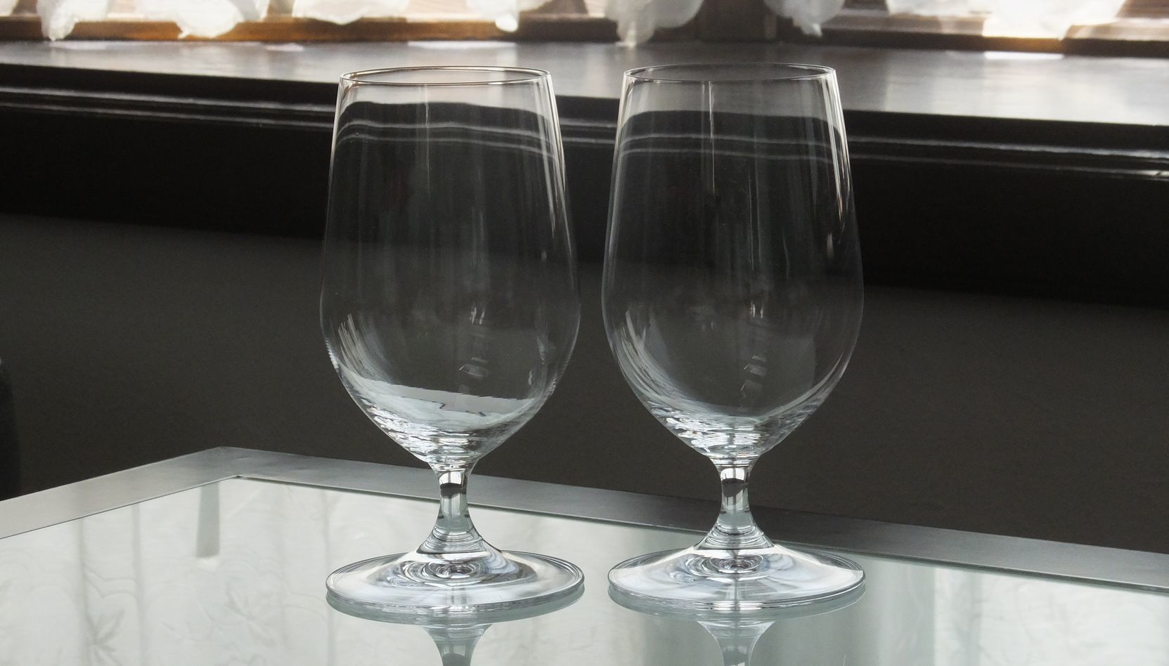 テーブルの上に並べられた、リーデル（RIEDEL）の『オヴァチュア ビアグラス』ペアの写真。ビールの豊かな泡立ちと香りを引き立てる洗練されたフォルムと透き通るクリスタルの輝きが美しく、日常の贅沢なひとときや結婚祝い、引っ越し祝いなどのカジュアルかつ上質なペアギフトにふさわしいイメージ。