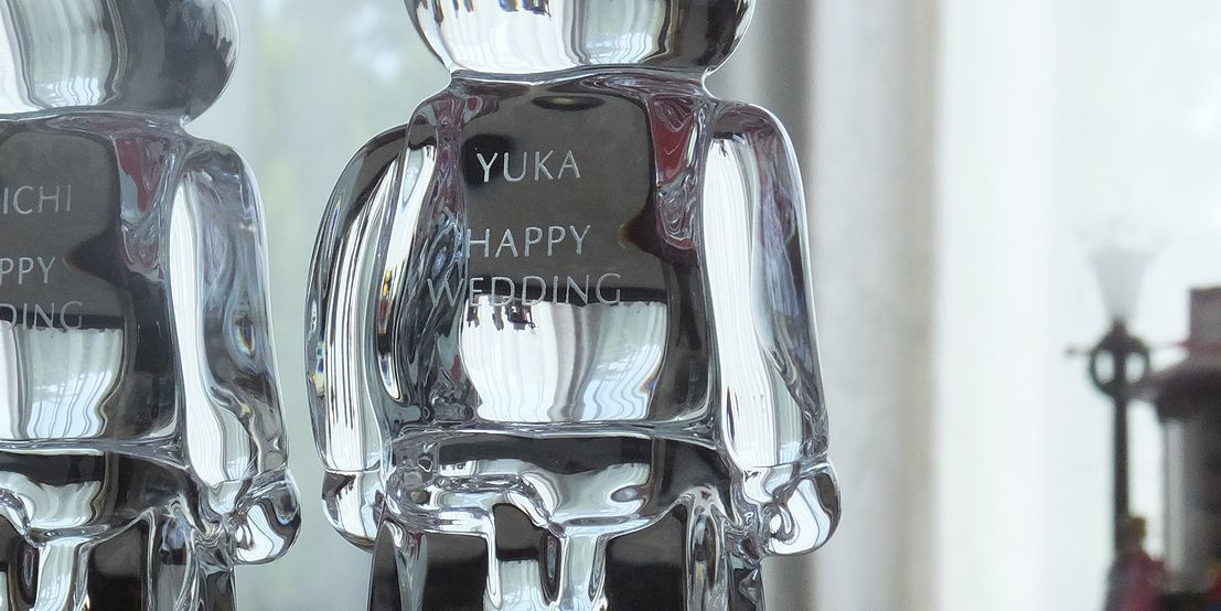 バカラのベアブリックの背中に、『YUKA HAPPY WEDDING』と名入れ彫刻したアップ写真。透明なクリスタルの背面に、お二人の幸せな結婚を祝うメッセージが繊細に刻まれ、世界に一つだけの特別なウェディングギフトとしての価値を高めています。