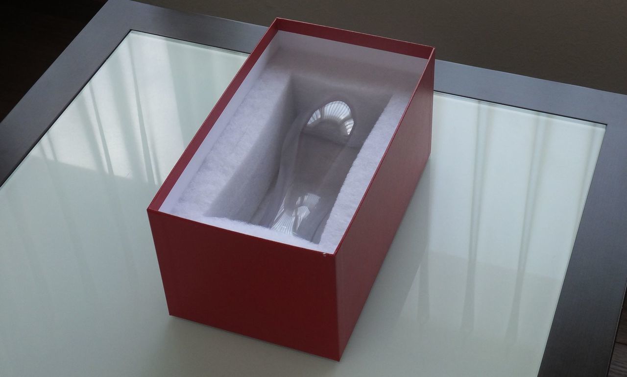バカラを象徴する鮮やかなレッドボックス（赤箱）の中に、美しく収められた『オノロジー』ビアタンブラーの写真。蓋を開けた瞬間に現れる、滑らかな曲線と圧倒的な透明感を誇る最高級クリスタルグラスが、ブランドの品格を物語る白いインナーサテンに包まれて気品高く佇んでいる。手にした瞬間の高揚感と贅沢な開封の歓びを予感させ、特別な記念日や大切な方への最高峰のギフトにふさわしい、ラグジュアリー感溢れるイメージ。
