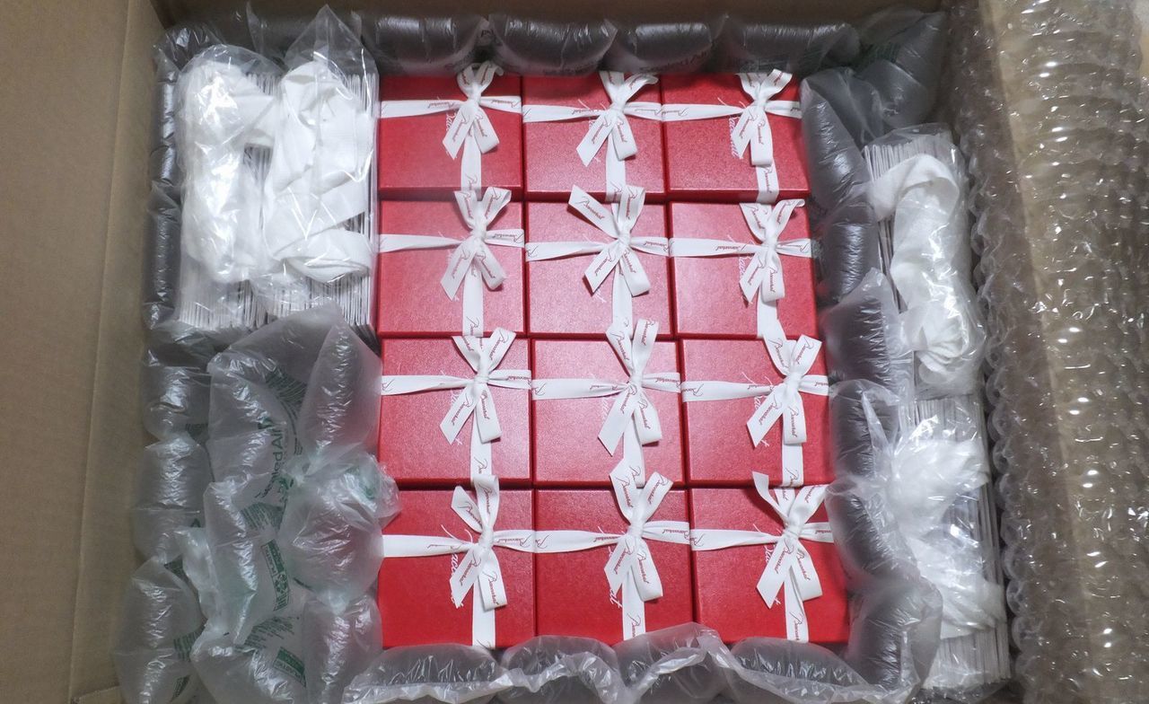 バカラグラスを安全かつ確実に配送するため、40個以上のグラスが緩衝材（プチプチや紙）を隙間なく敷き詰めた大きな段ボール箱に整然と梱包されている写真。高額なクリスタル製品の輸送中の破損を厳重に防ぐためのプロフェッショナルな梱包技術と、大量注文への対応力を伝える情景。