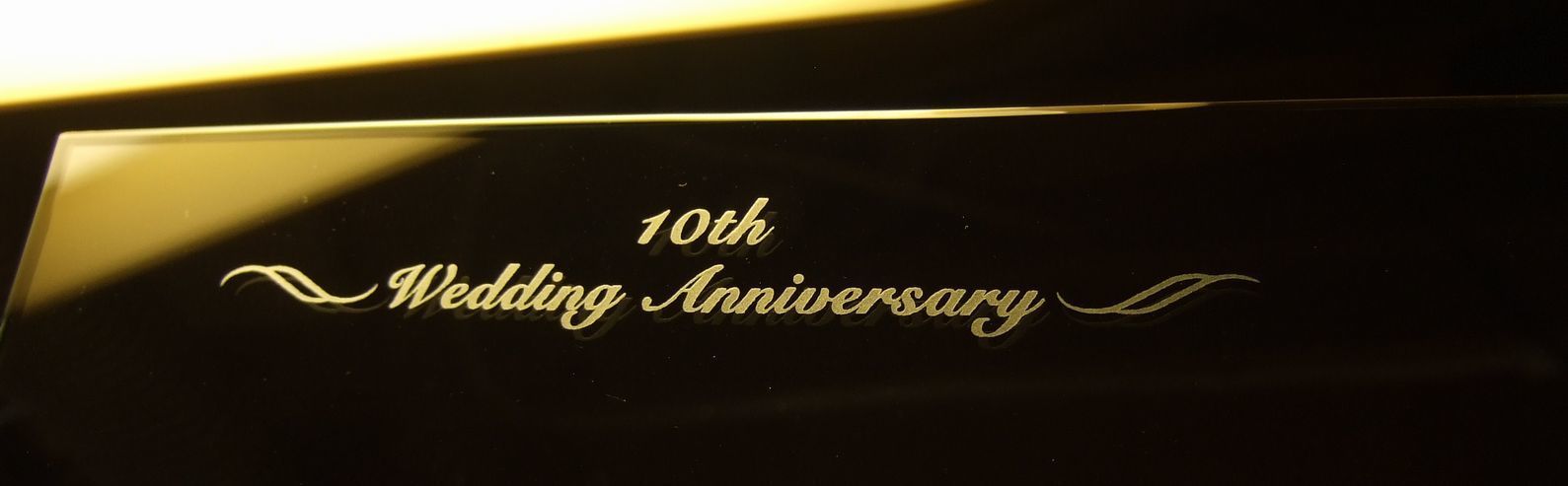 グラスワークスナルミのフォトフレームに『10th wedding anniversary』と名入れ彫刻が施された写真。文字の左右には美しい装飾デザインが施され、特別な記念日を祝う贈り物としての高級感を表現