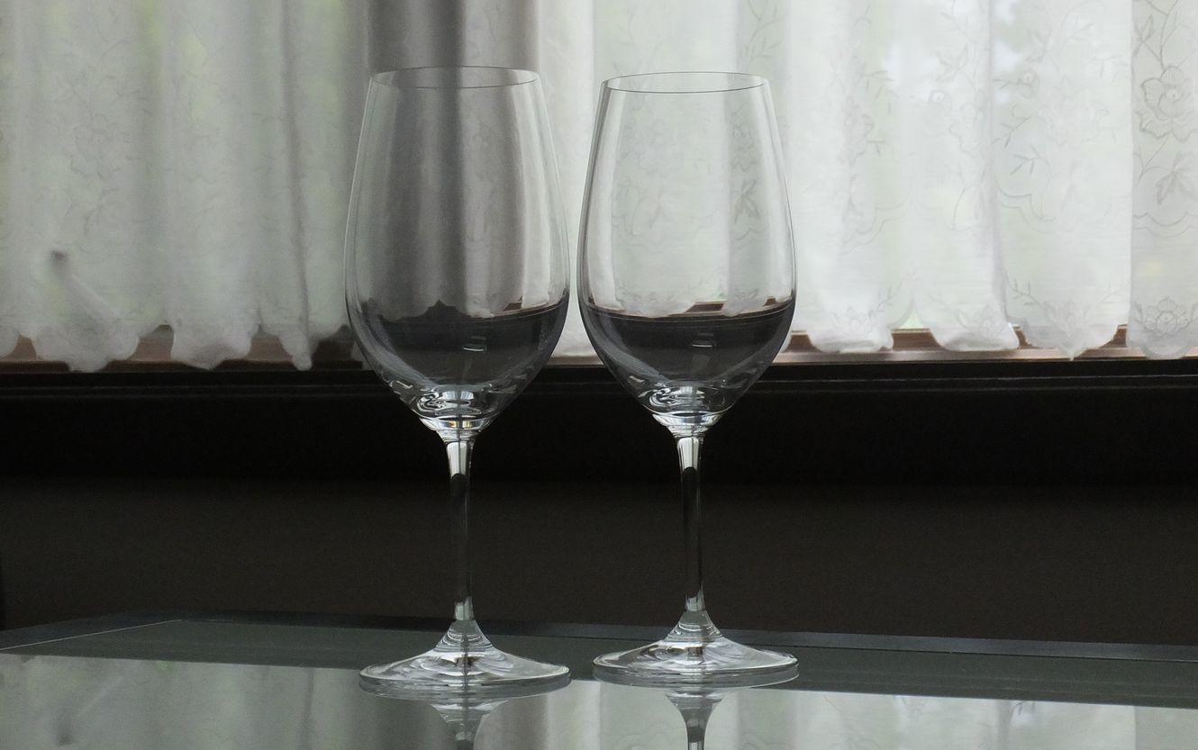 洗練されたテーブルの上に並べて置かれた、リーデル（RIEDEL）の『ヴィノム』シリーズ、リースリング・グラン・クリュのペアワイングラスの写真。縦長でやや小ぶりな卵型のボウルが特徴の最高級クリスタルグラス。白ワインのフレッシュな酸味とフルーティーなアロマを最大限に引き出すために計算された機能美あふれるフォルムが美しく、光を受けて透明感のある輝きを放つ、結婚祝いや記念日の特別なギフト、上質なペアディナーの空間を優雅に彩るイメージ。