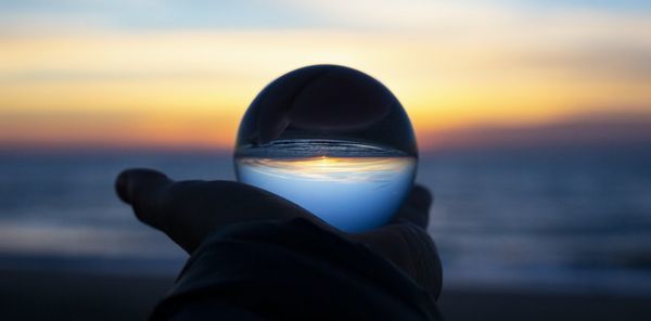 海が見える浜辺で手のひらに水晶を持ち、夕陽の光が反射して輝く美しいシーン。自然の美しさとともに、価値のあるもの、美しいものの本質を感じさせる瞬間