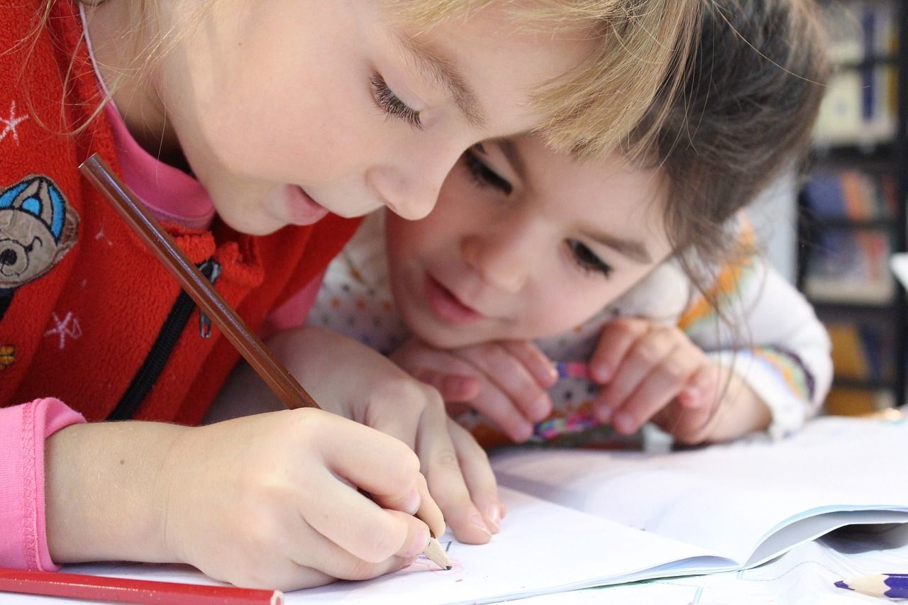 仲良く並んでノートに鉛筆で書き込む二人の小学生の女の子。笑顔で楽しく勉強している姿が伝わる学習シーン