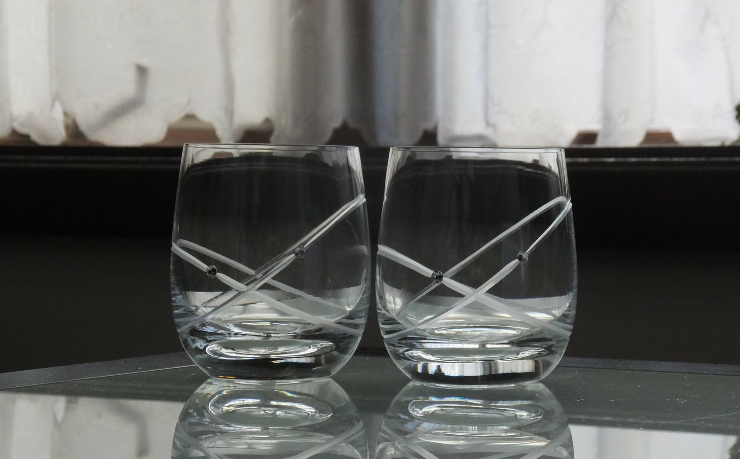 ウェッジウッド（WEDGWOOD）のクリスタルタンブラー、プロミシス（Promesis） ウィズディスリング リングタンブラーのペアセットが、テーブルの上に並べて置かれている写真。タンブラーの上部には、結婚の誓いを象徴する二重のリング（輪）状の繊細なカットが施されており、シンプルながらもエレガントなデザインが際立っている。夫婦の絆を表現した美しいクリスタルが、光を優しく反射させ、結婚祝いや記念日にふさわしい洗練されたペアギフトの情景。