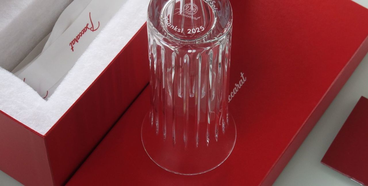 バカラの花瓶、フローラ ベースのクリスタル製フラワーベースのクローズアップ写真。なめらかな曲面と丸みを帯びた優美なフォルムが特徴の花瓶の底面中央に、退職祝いのメッセージとして『Thanks! 2025』という感謝の言葉と記念の年が名入れ彫刻されているのが鮮明に確認できる。重厚なクリスタルの底面に施された控えめながらも心温まるメッセージが、長年の功績と感謝の気持ちを伝える特別な退職記念品