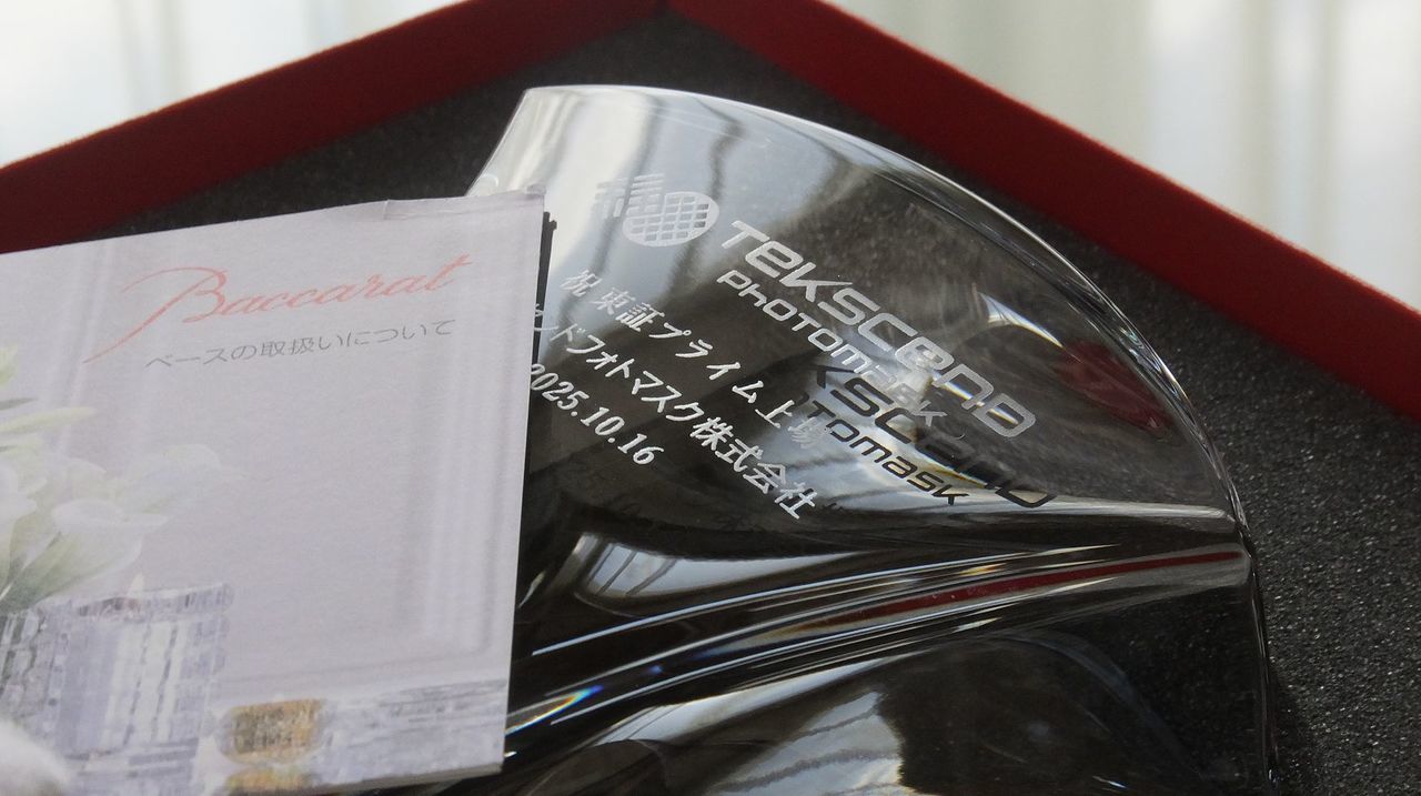 バカラの花瓶、ギンコ ベースのクリスタル製フラワーベースのクローズアップ写真。イチョウの葉（ギンコ）をモチーフとしたダイナミックな曲面が特徴の花瓶の側面中央に、上場祝いのメッセージとして『祝 東証プライム上場』、『[企業名]』、『2025.10.16』、そして『企業ロゴ』が名入れ彫刻されているのが鮮明に確認できる。重厚で透明度の高いクリスタルが、企業の大きな成功と輝かしい未来を象徴する最高峰の記念品。