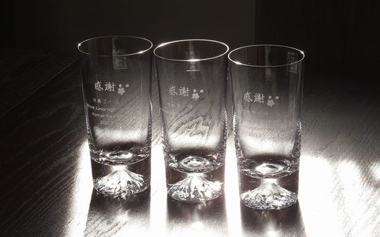 田島硝子の富士山ハイボールグラス3脚が並び、それぞれの側面に感謝の文字、桜の花びらのデザイン、お名前、そして感謝のメッセージと学校名、日付が名入れ彫刻された、卒業記念や退職祝いに最適な、特別なギフトの写真。