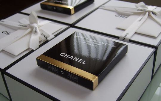 シャネルの名入れコンパクトミラーがギフトボックスの上に並び、洗練された贈り物の雰囲気を醸し出す。高級感と上品さが際立つ、特別なプレゼントに最適なアイテム。