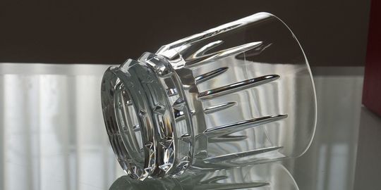 バカラのタンブラー（ロックグラス）の名入れページの商品一覧で使用する写真。バカラ アルルカンタンブラーがテーブルの上に置かれています。斜めの格子状のカットが特徴的なグラスが光を反射して輝き、名入れギフトとしてのモダンアートのような洗練された美しさと特別感を演出しています。