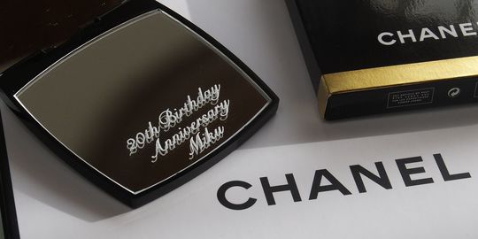 シャネルのコンパクトミラーに“20th birthday anniversary”と名前を名入れ彫刻した写真。エレガントなブラックのミラー表面に記念の文字が美しく刻まれ、大切な20歳の誕生日を祝う特別なプレゼントに仕上げられた記念アイテム