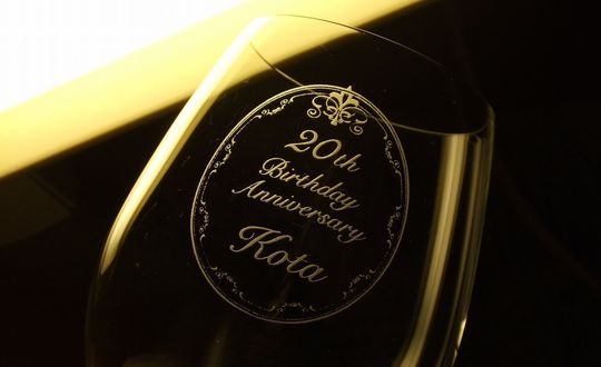 リーデル オヴァチュアレッドワイングラスの側面に、２０歳祝いのメッセージと名前をデザインした名入れ彫刻を施した写真。特別な記念日を祝うためのエレガントなギフトで、リーデルの優れた品質と美しいデザインが際立つ一品