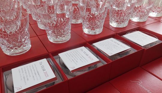 バカラのアリア（Aria）タンブラー2025が、品質管理または検品作業のために、真紅のオリジナルボックスの上に50個以上、整然と規則正しく並べて置かれている集合写真。雪の結晶を思わせる繊細なカットが施されたグラスが、均一な配置と光の反射により壮観な輝きを放っている。クリスタル製品の最高品質を保つための厳格なチェックを象徴する情景であり、大量注文の完璧な仕上がりを伝える。