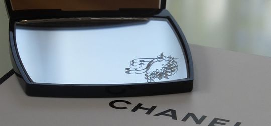 シャネルのコンパクトミラーの下部ミラーに、エレガントなバラの装飾とイニシャル『T』を名入れ彫刻した写真。華やかで繊細なデザインが高級感を醸し出す、特別なギフト仕様のイメージ。