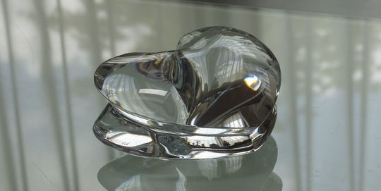 バカラの招き猫 クリアMサイズがテーブルの上に置いてある写真。透明なクリスタル製の招き猫が、その美しいフォルムと光の反射で、空間に幸運と洗練された雰囲気をもたらしています。名入れギフトとしても、インテリアとしても魅力的な逸品です。