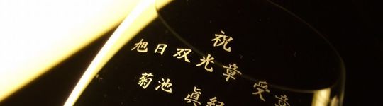 旭日双光章の受章を祝う名入れ彫刻入りグラス。側面に“祝 旭日双光章 受章”と受章者の名前を刻んだ記念品