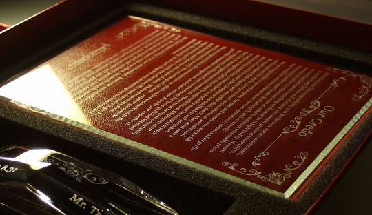 バカラのクリスタル製写真立て、アビス（Abysse）フォトフレームのクローズアップ写真。深海を思わせる大胆な四角錐のカットを持つ重厚なフレーム部分（前面または側面）に、退任祝いとして長文の英文で構成された企業理念が、緻密に名入れ彫刻されているのが鮮明に確認できる。透明度の高いクリスタル全面を埋め尽くす長文のメッセージが、長きにわたる経営への貢献と企業への深い敬意を象徴する格調高いオーダーメイドギフト。