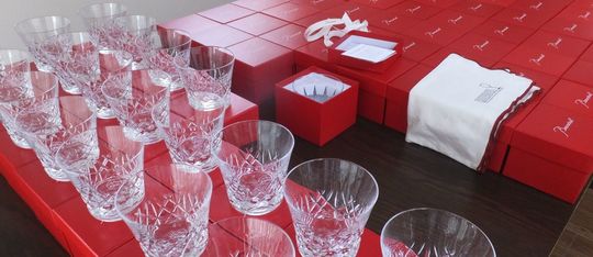 バカラのアリア（Aria）タンブラー2025が、品質管理または検品作業のために、真紅のオリジナルボックスの上に50個以上、整然と規則正しく並べて置かれている集合写真。しずくを思わせる繊細なカットが施されたグラスが、均一な配置と光の反射により壮観な輝きを放っている。クリスタル製品の最高品質を保つための厳格なチェックを象徴する情景であり、大量注文の完璧な仕上がりを伝える。