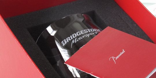 バカラのタンブラー（ロックグラス）の名入れページの商品一覧で使用する写真。シャトーバカラタンブラーの側面に、『BRIDGESTONE motor sport』のロゴデザインを名入れ彫刻した写真。丸みを帯びた優雅なフォルムのクリスタルに、力強いモータースポーツのロゴが美しく刻まれ、企業やイベントの特別な記念品としての高級感と、洗練されたデザインが融合した逸品です。