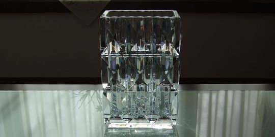 バカラのルクソールスクウェアベースがテーブルの上に置いてある写真。ピラミッドのような幾何学的なカットが特徴のベースが、光を反射して輝き、名入れギフトとしてのモダンで力強い存在感と、空間を彩る洗練された美しさを演出しています。