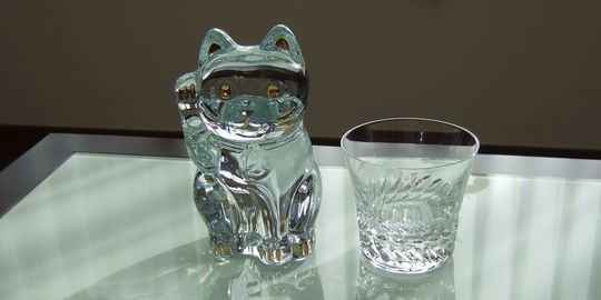 バカラの招き猫 クリアMサイズがテーブルの上に置いてある写真。透明なクリスタル製の招き猫が、その美しいフォルムと光の反射で、空間に幸運と洗練された雰囲気をもたらしています。名入れギフトとしても、インテリアとしても魅力的な逸品です。