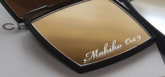 シャネルのミラー下部に、流麗なスクリプト体（筆記体）で『Makiko Oct 9』と名入れ彫刻を施した写真。お名前と記念日が美しく刻印された、エレガントで特別感あふれるパーソナライズギフトのイメージ。