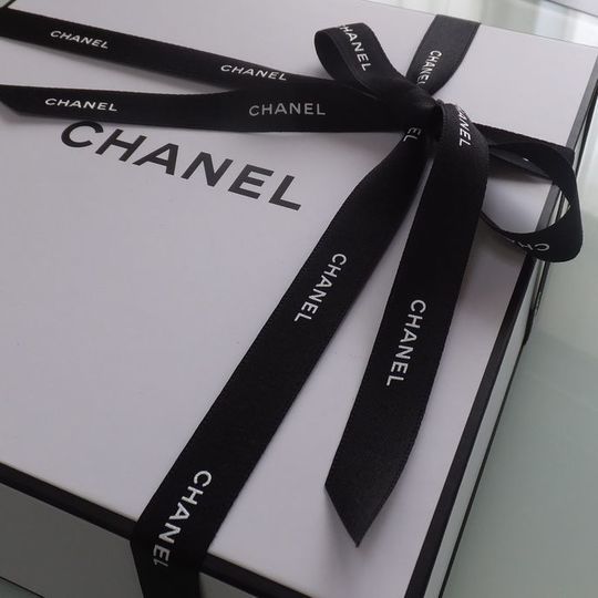 黒いシャネルのリボンが付いた特別仕様のギフトボックスに包まれたシャネルコンパクトミラー。エレガントで上品なデザインが際立つ贈り物。